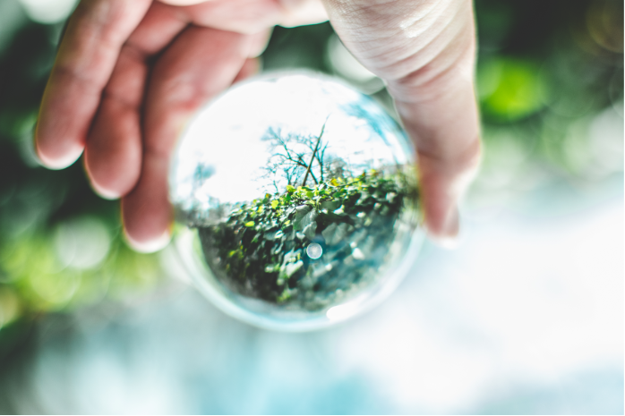 una mano sosteniendo una bola de cristal en la que se ve el reflejo de un paisaje natural