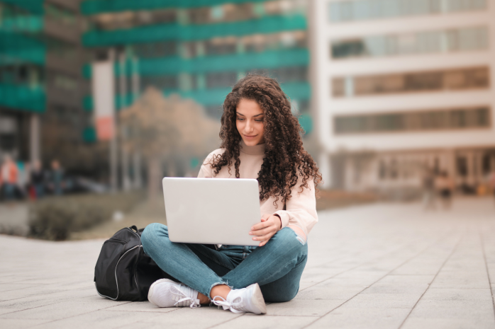 una joven sentada en el suelo de una calle de una ciudad con un ordenador portátil