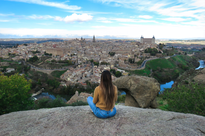 una joven sentada con la ciudad de Toledo de fondo