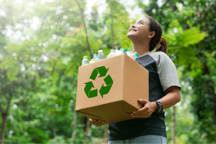 una chica con una caja con el logo del reciclaje llena de botellas de plástico