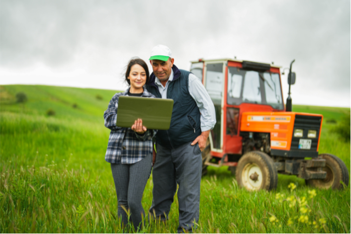 una mujer y un hombre consultando un portátil en un campo frente a un tractor