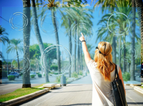 Una mujer con unas gafas de realidad virtual toca una pantalla con una imagen de fondo de un paseo con palmeras