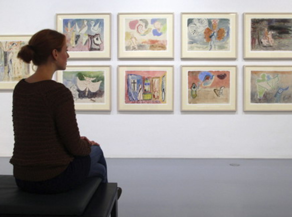 Una mujer sentada en un banco contempla unos cuadros en un museo