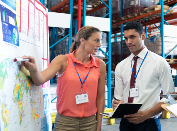 Una mujer en un almacén explica con un mapa a su equipo la distribución a otros países de una mercancía