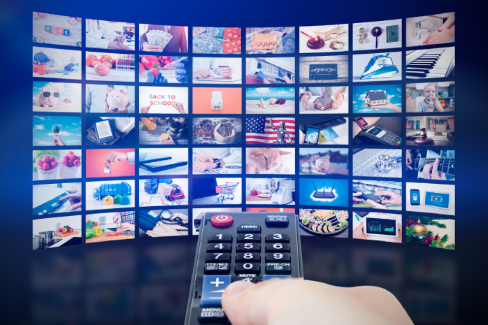 Una mano con un mando de televisión frente a varias pantallas con distintos canales sintonizados