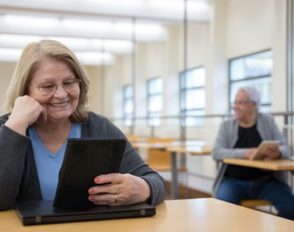 dos personas mayores con dispositivos digitales en un aula