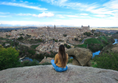 Una joven sentada de espaladas y admirando una panorámica de Toledo