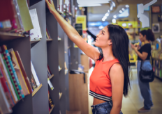 una joven en una librería cogiendo un libro de una estantería