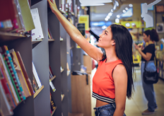 una joven cogiendo un libro de una estantería en una libreria