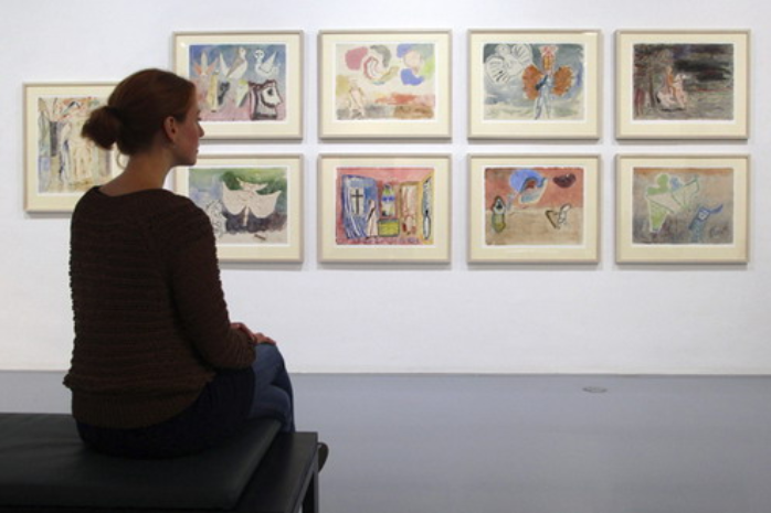 Una mujer sentada en un banco contempla unos cuadros en un museo
