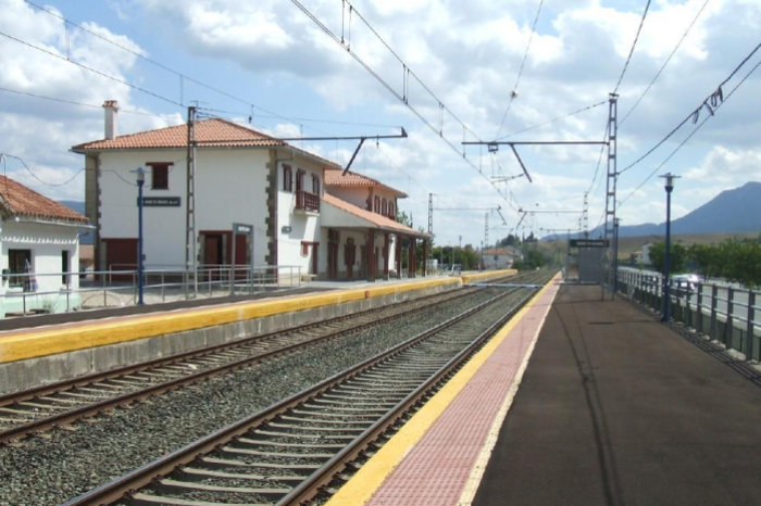 Tramo de la vía del tren con un apeadero en el fondo.
