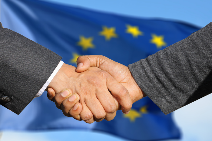 dos personas dándose la mano. al fondo una bandera de la UE